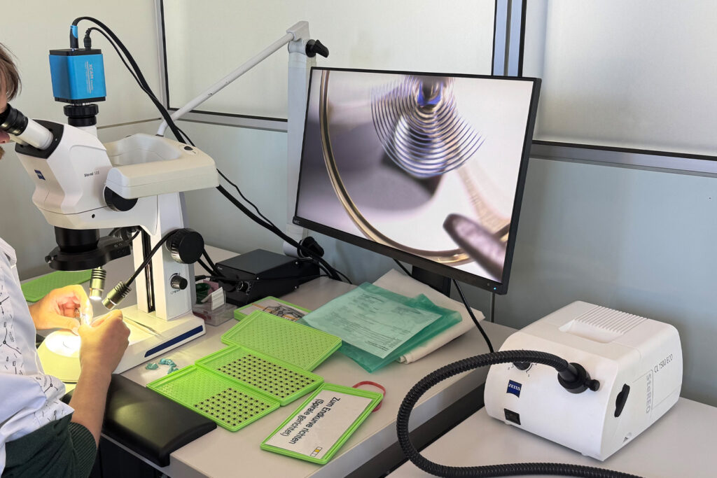 Adjusting the balance spring at Nomos Glashütte, man sitting at a microscope in front of a screen