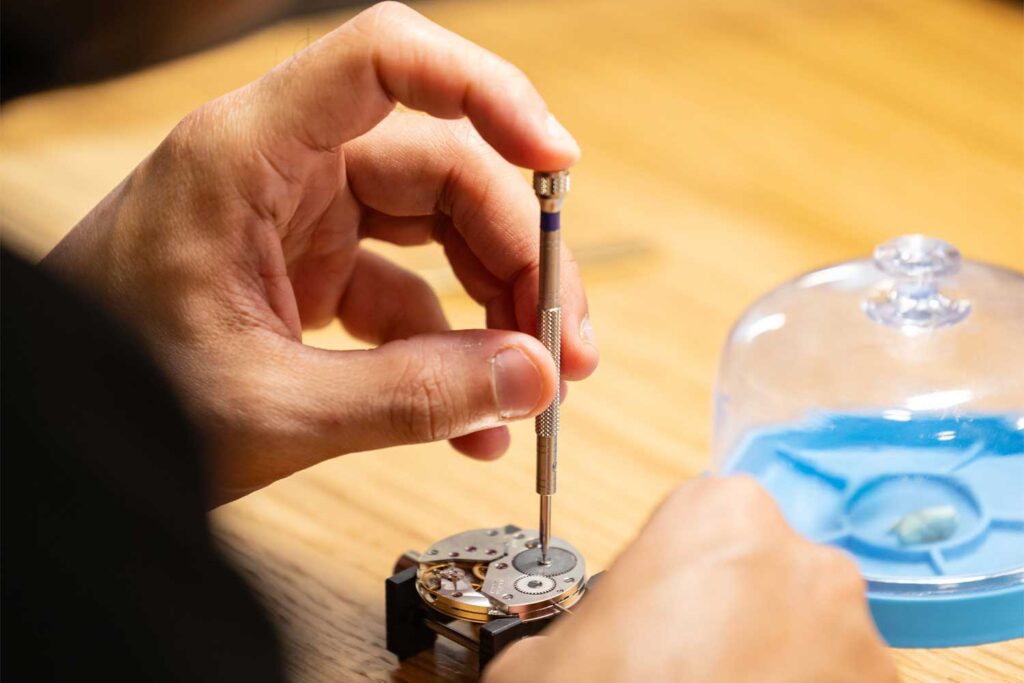 Hand hält einen Uhrmacher-Schraubendreher an ein Uhrwerk auf der Watches & Wonders Geneva