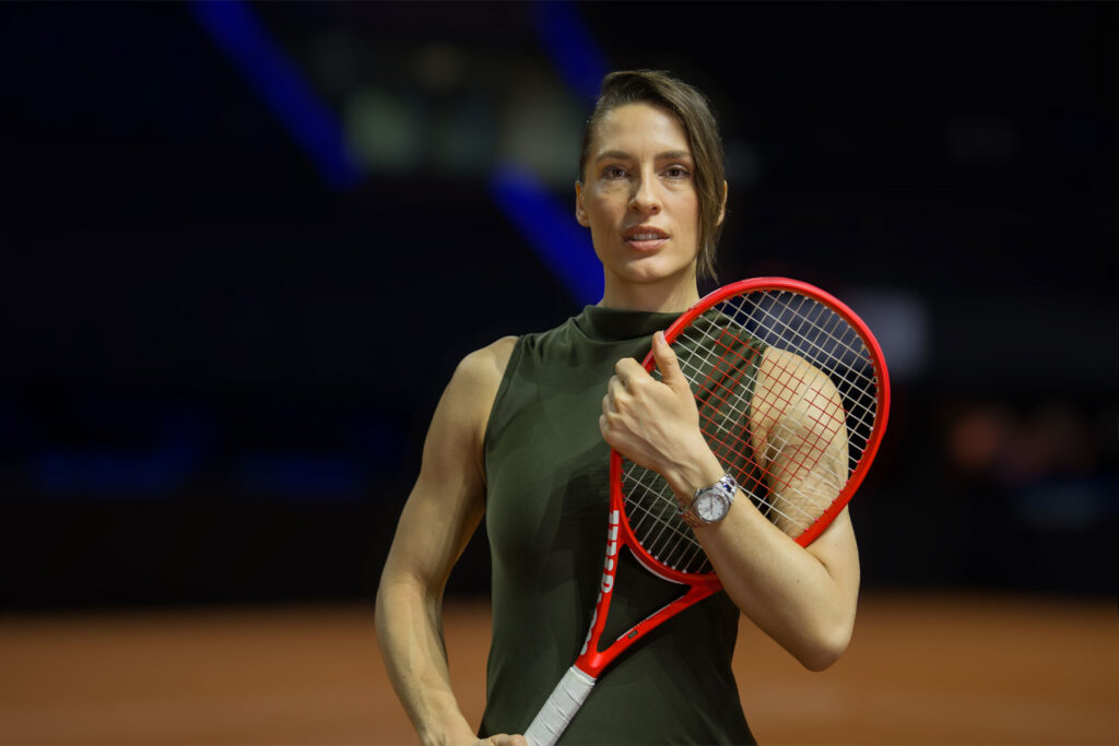 Andrea Petković steht auf einem Tennisplatz am Netz und trägt eine Sky von Tutima