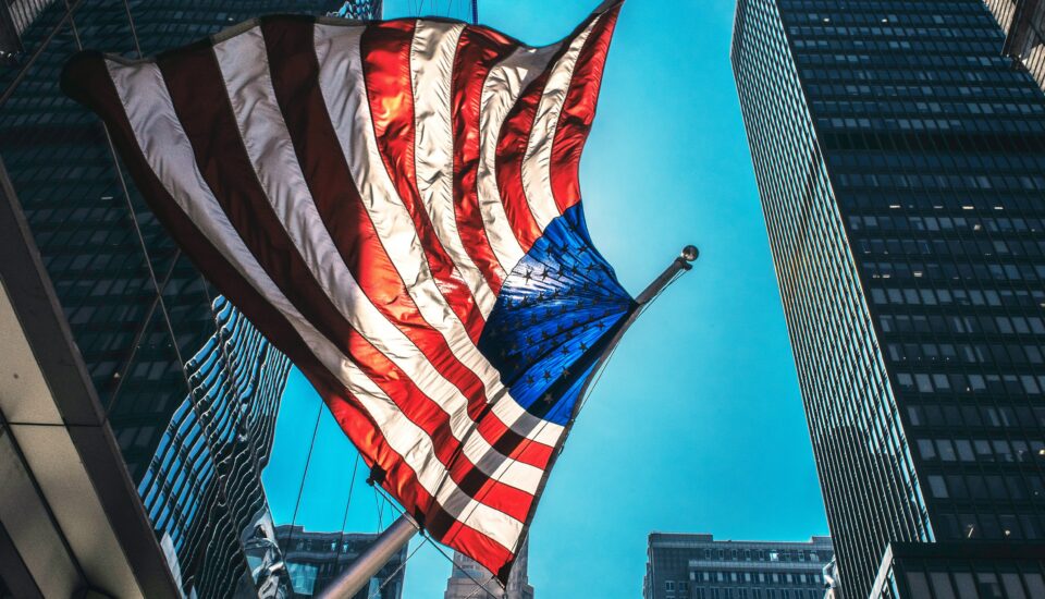 US-Amerikanische Flagge vor urbanem Hintergrund mit blauem Himmel