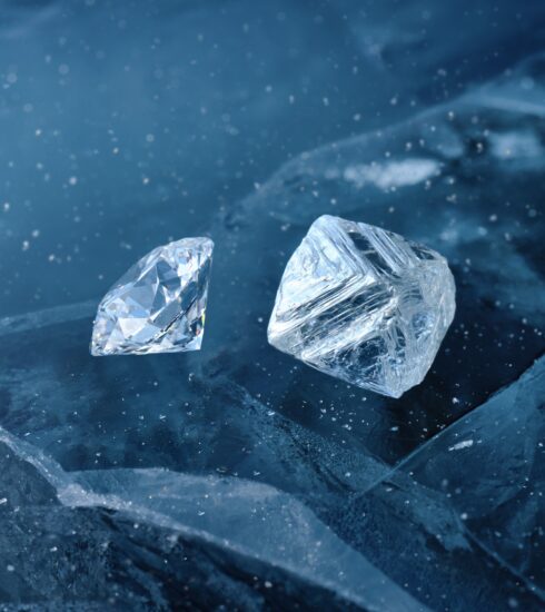 Ein geschliffener Diamant und ein ungeschliffener Rohdiamant unter Wasser umgeben von Eisschollen.