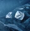 Ein geschliffener Diamant und ein ungeschliffener Rohdiamant unter Wasser umgeben von Eisschollen.