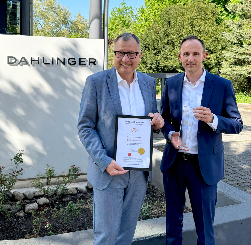 Bernd Dahlinger erhält die Urkunde des Hidden Champion von Dominik Fehringer. Beide stehen vor dem Dahlinger Firmenschild