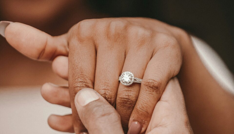 Lächelnde Frau zeigt Verlobungsring aus weißen Diamanten an ihrer Hand.