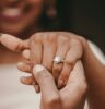 Lächelnde Frau zeigt Verlobungsring aus weißen Diamanten an ihrer Hand.