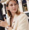 Blondes Model hält vor ihrem Körper eine Damendarmbanduhr mit rechteckigem Gehäuse und braunem Zifferblatt.