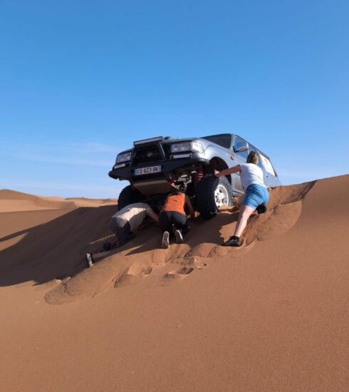 Geländefahrzeug hat sich auf einer Sanddüne in der Wüste festgefahren, mehrere Personen versuchen, das Fahrzeug freizuschaufeln