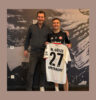 Tim Stracke and Mario Götze are standing next to each other; Mario Götze is holding a signed football jersey with the number 27.
