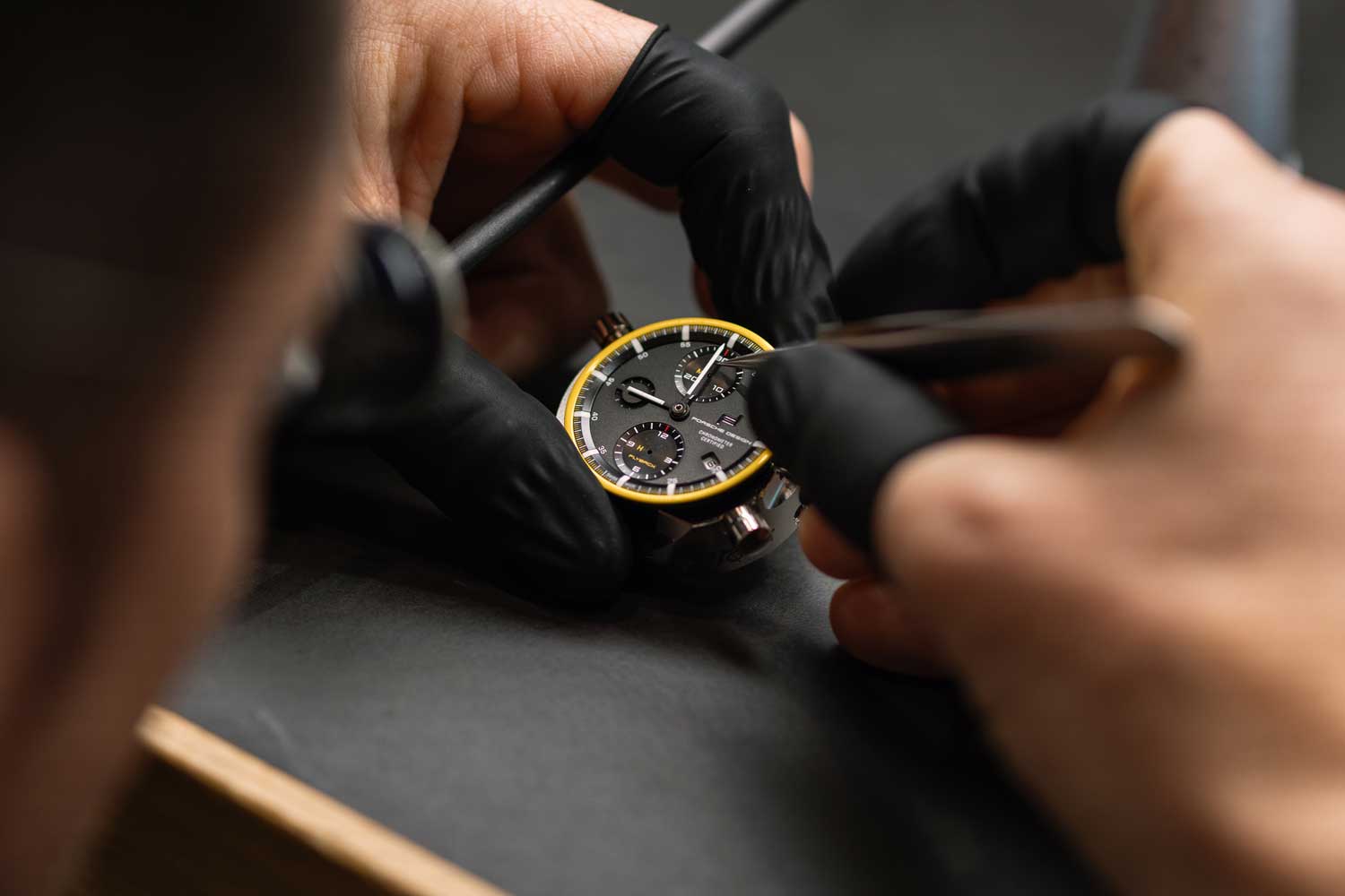 Two hands wearing finger cots hold a watch head