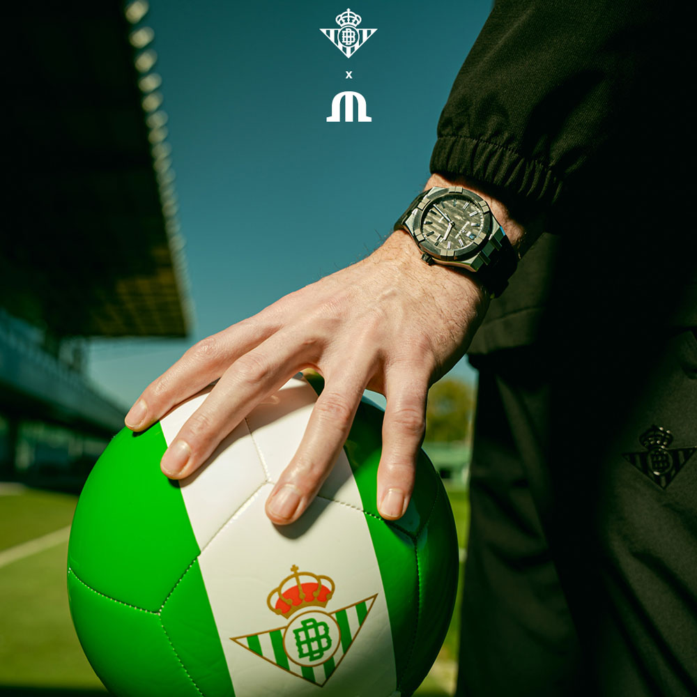 Eine Hand mit einer Aikonic von Maurice Lacroix am Handgelenk liegt auf einem Fußball der spanischen Mannschaft Real Betis Balompié