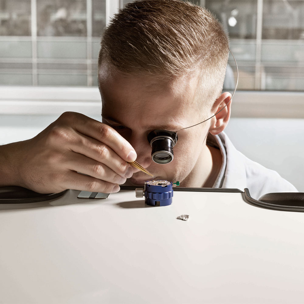 Ein Uhrmacher mit Uhrmacherlupe begutachtet ein Uhrwerk von Rolex